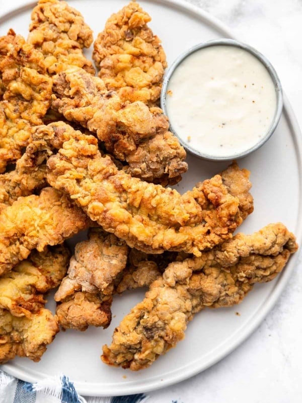 Steak fingers on a round plate with dipping sauce on side.