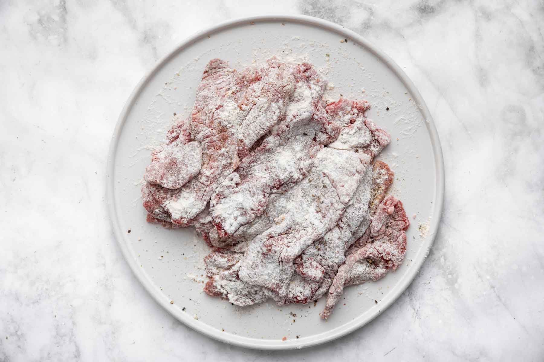Strips of meat coated in flour on white plate.