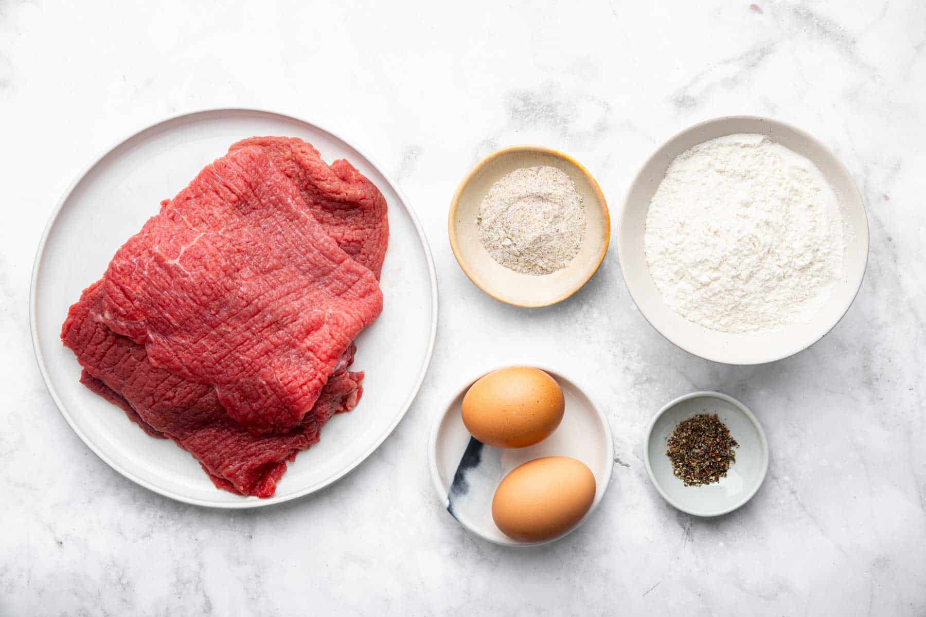 Bowl of cubed steak, eggs, flour and seasonings.