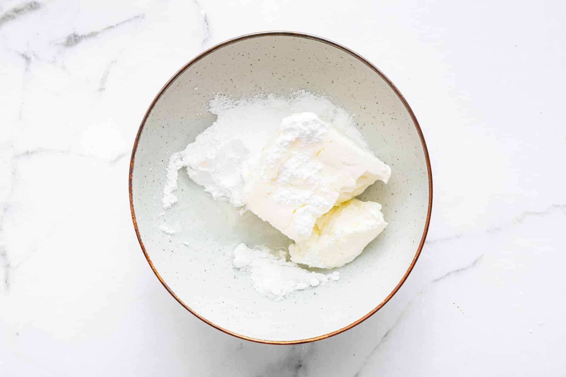 White bowl with cream cheese, sugar and lemon juice inside.