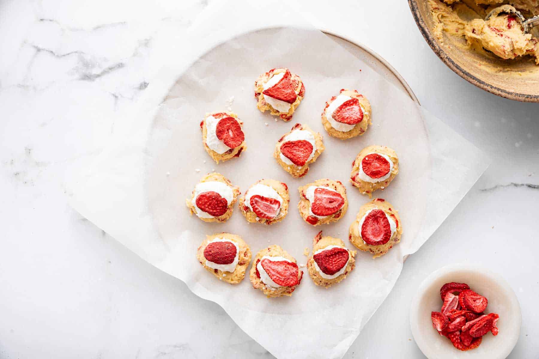 Strawberry cheesecake cookies being stuffed with white cream, before being baked.