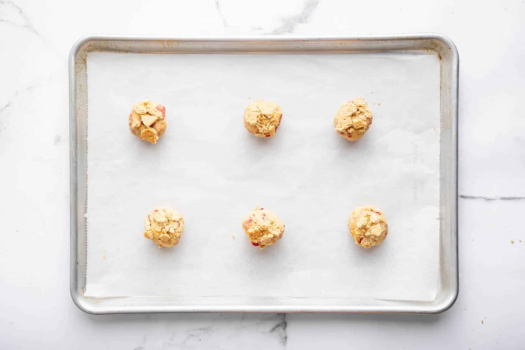 Six strawberry cheesecake cookies on a parchment lined baking sheet.