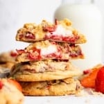 Stack of strawberry cheesecake cookies with top one cut in half to show white inside.