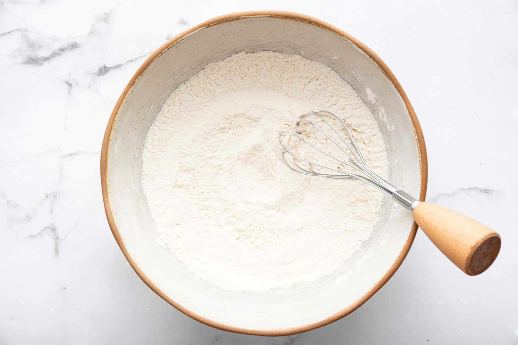 White bowl with flour and whisk inside.