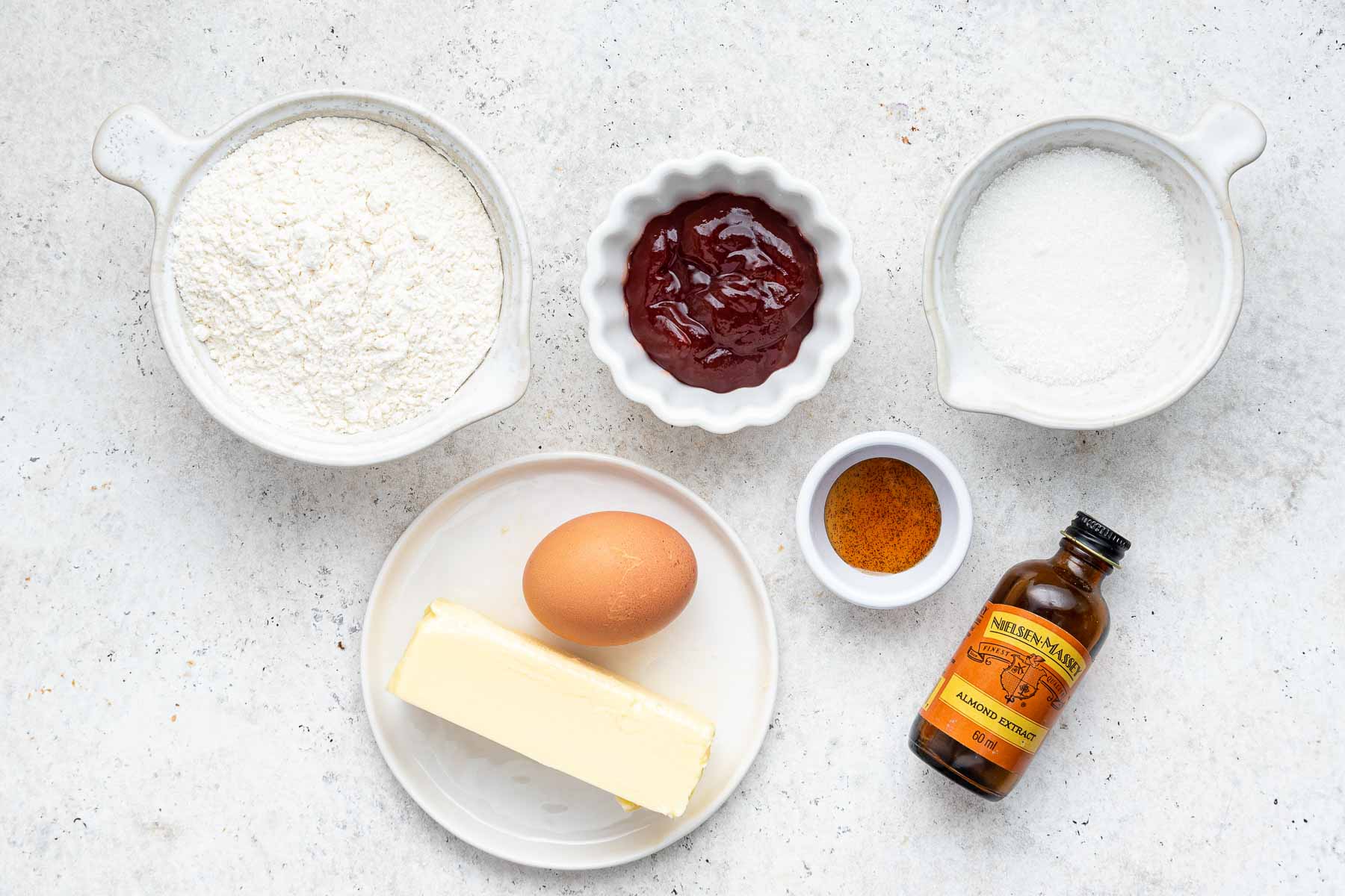 Bowls of flour, sugar, butter and egg on white surface.