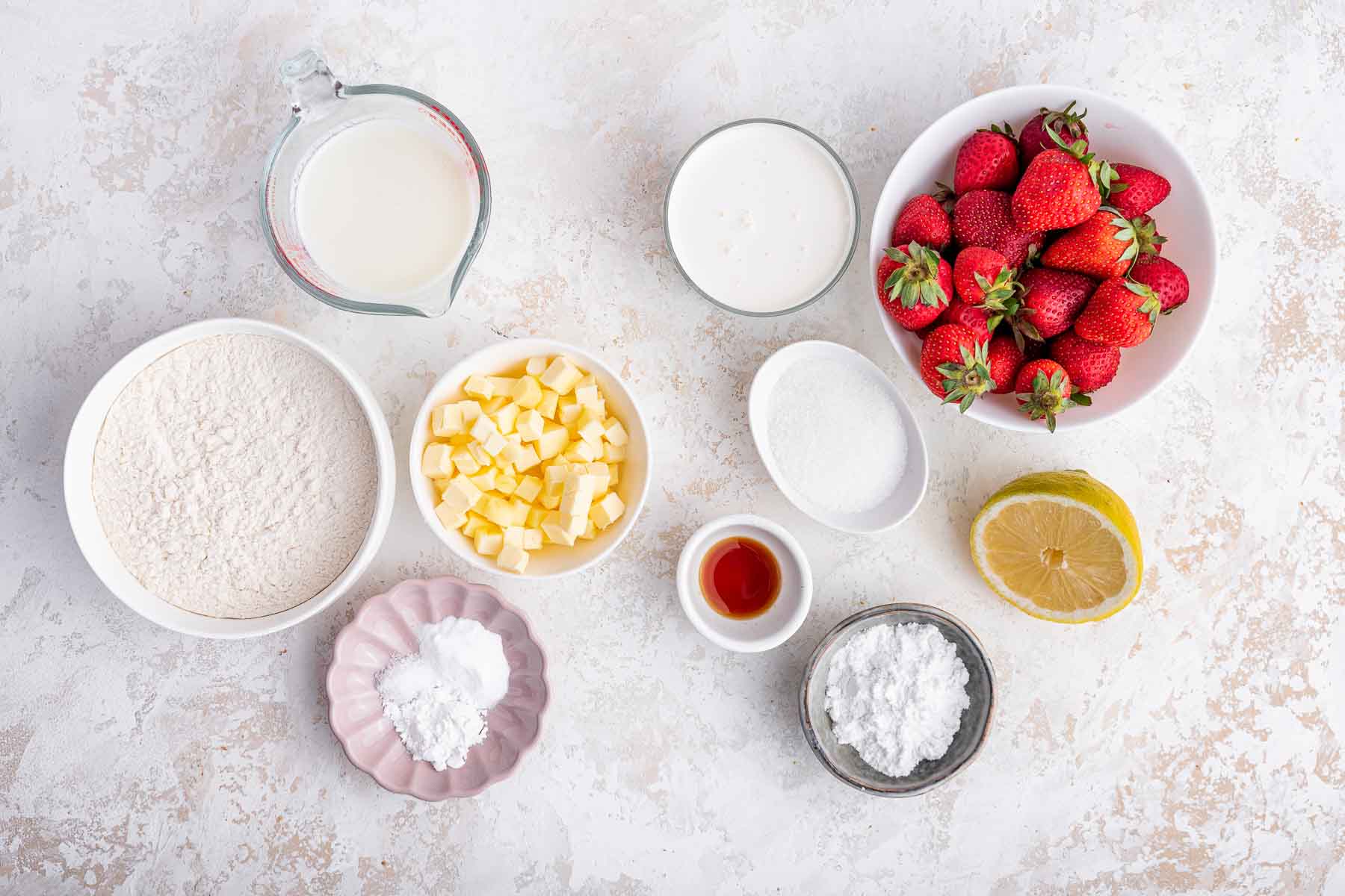 Bowl of flour, butter, sugar, and strawberries on white counter.