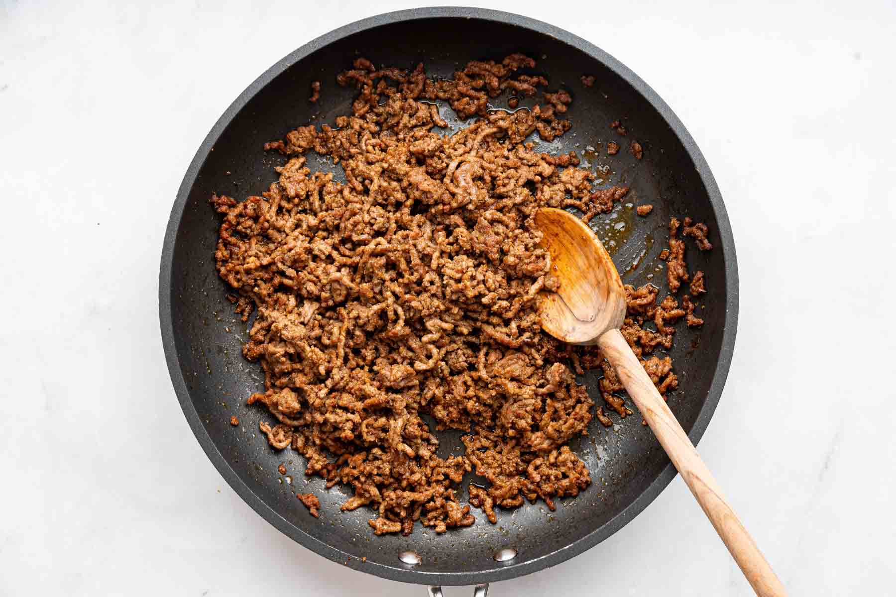 Taco meat in a skillet with wooden spoon.
