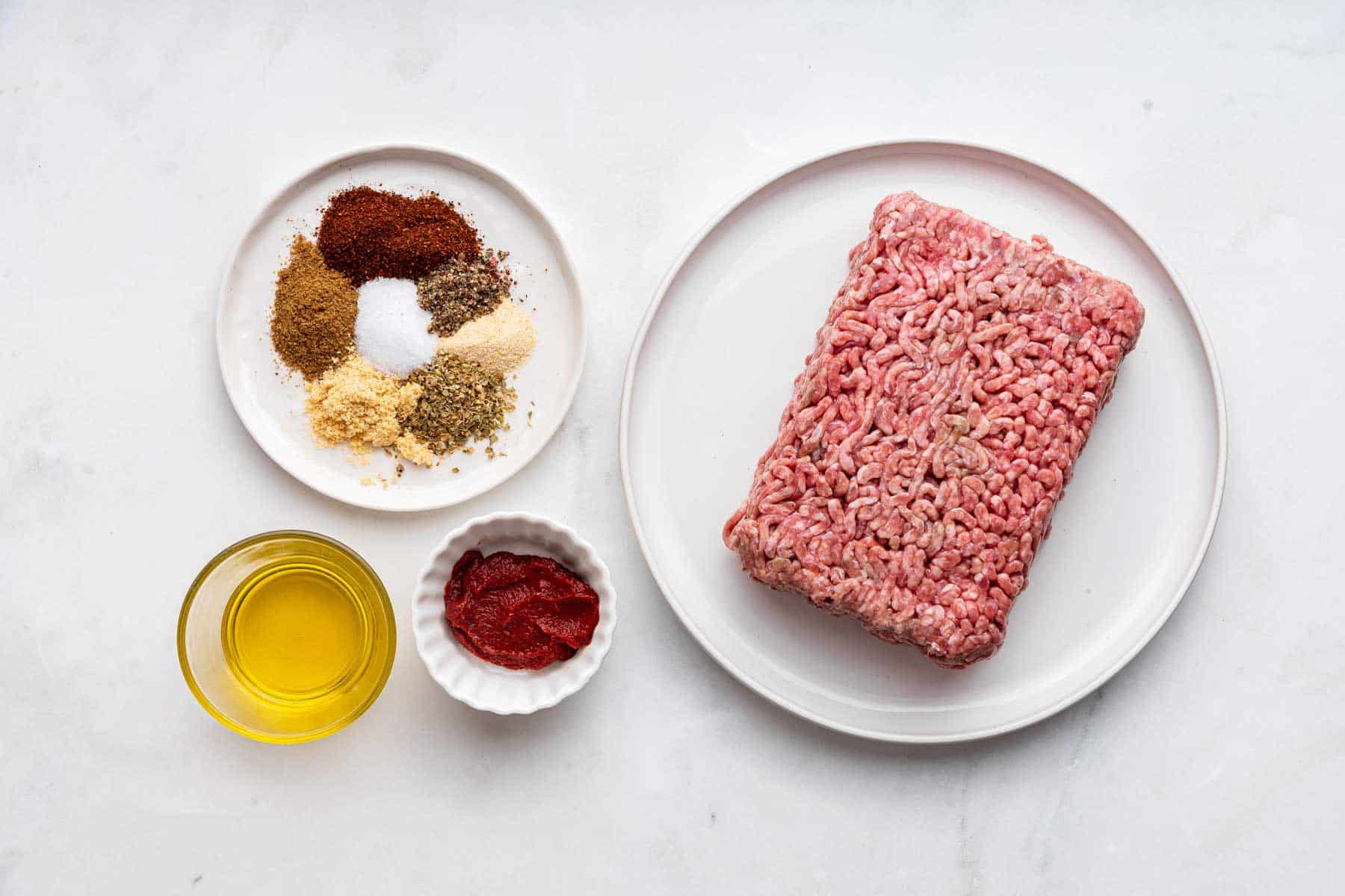 Raw ground beef and spices on two small plates.