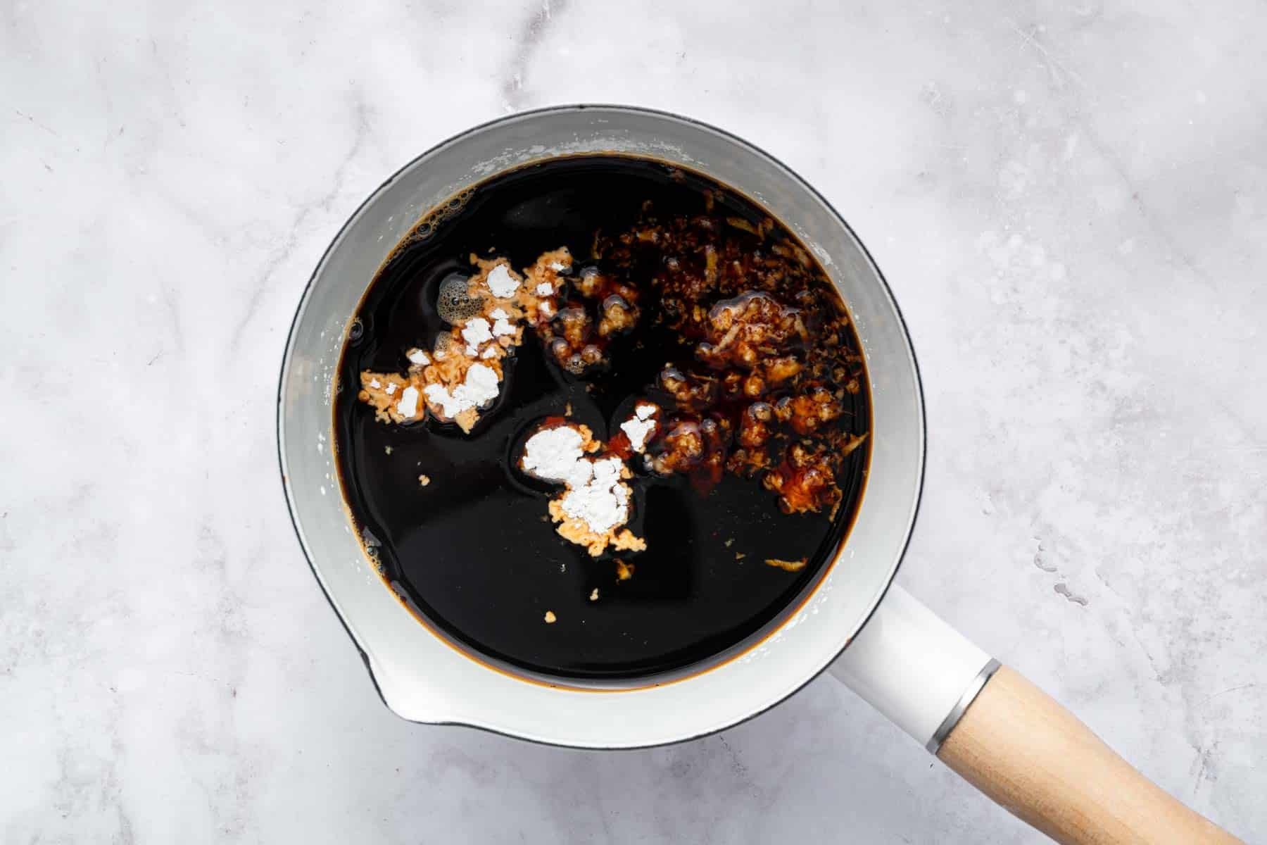 Brown liquid in white cooking pot with grated garlic and sugar on top.