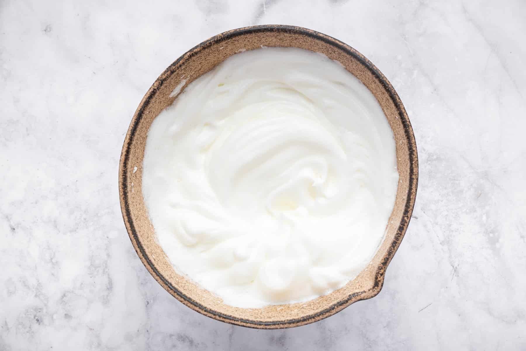 Brown bowl with beaten egg whites in it.