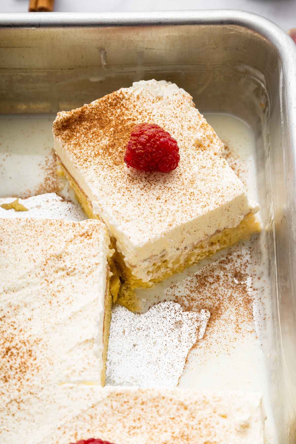 Slice of tres leches cake in pan with milk around the edges.