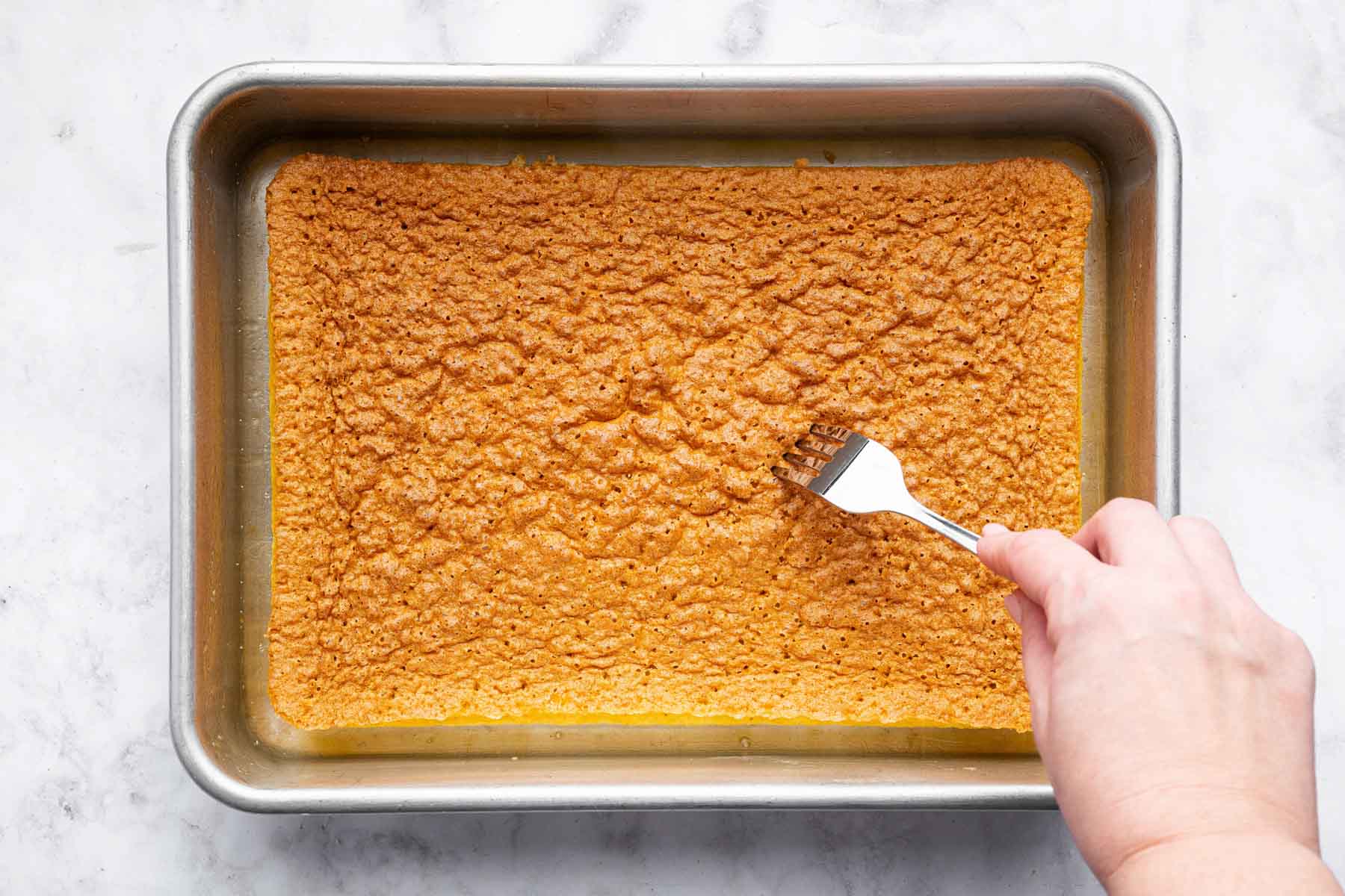 Hand using a fork to poke holes in a sponge cake.