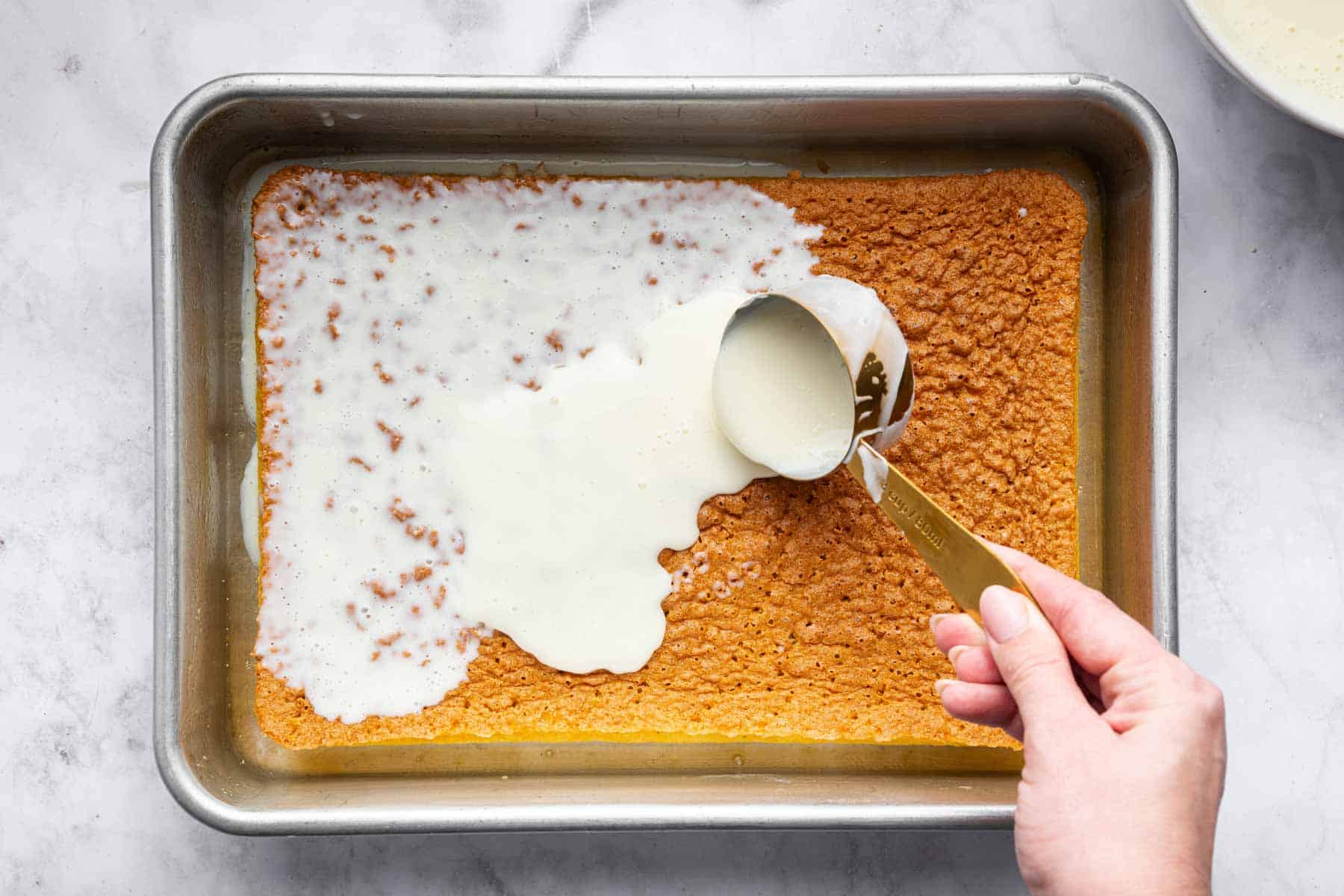 Measuring cup pouring milk over sponge.