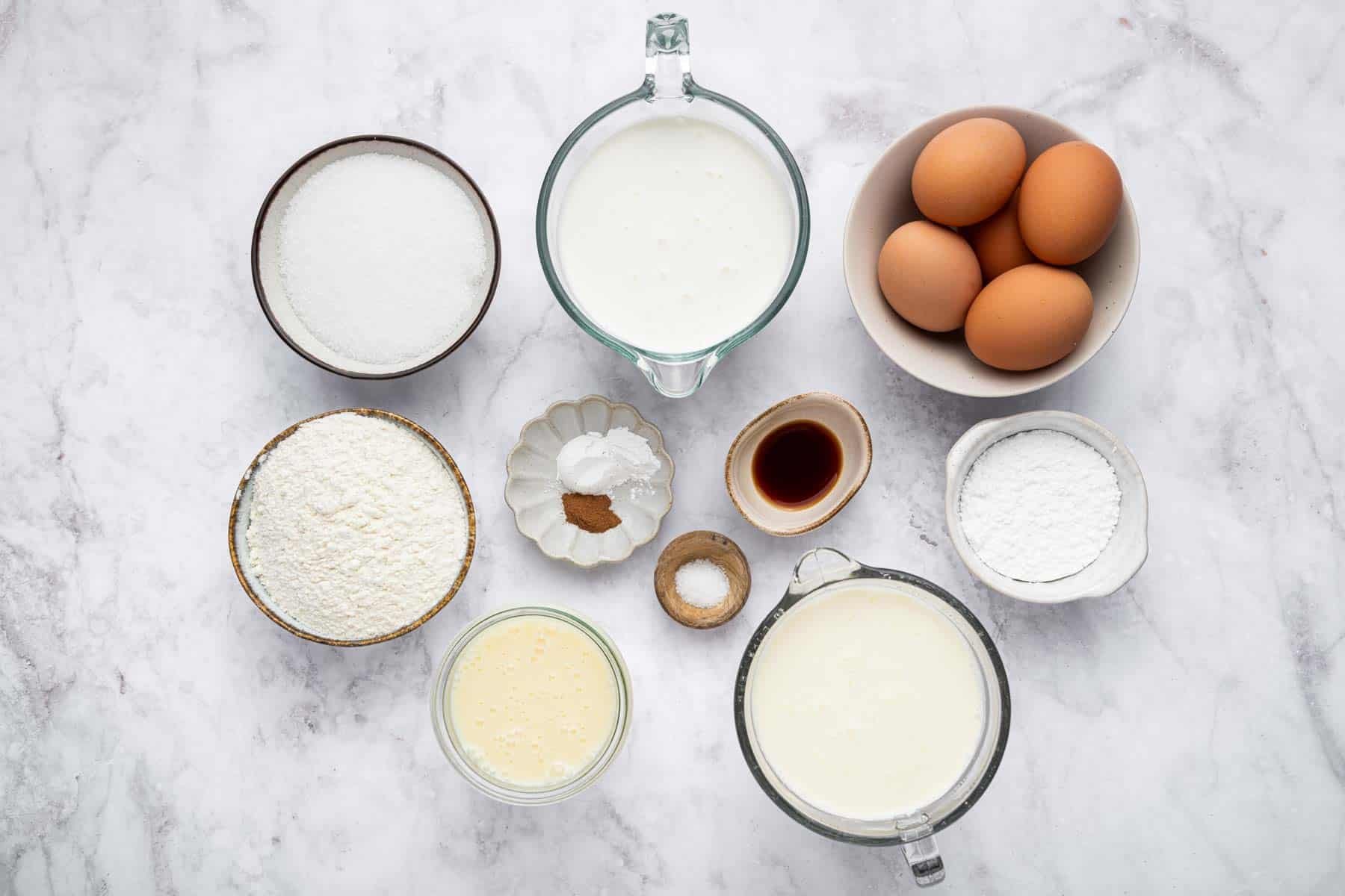 Bowls of milk, 4 eggs, vanilla, and salt on marble counter.