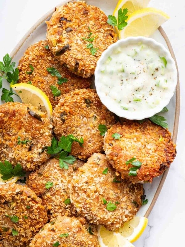 Vertical image of tuna patties on plate with bowl of ranch on the side.