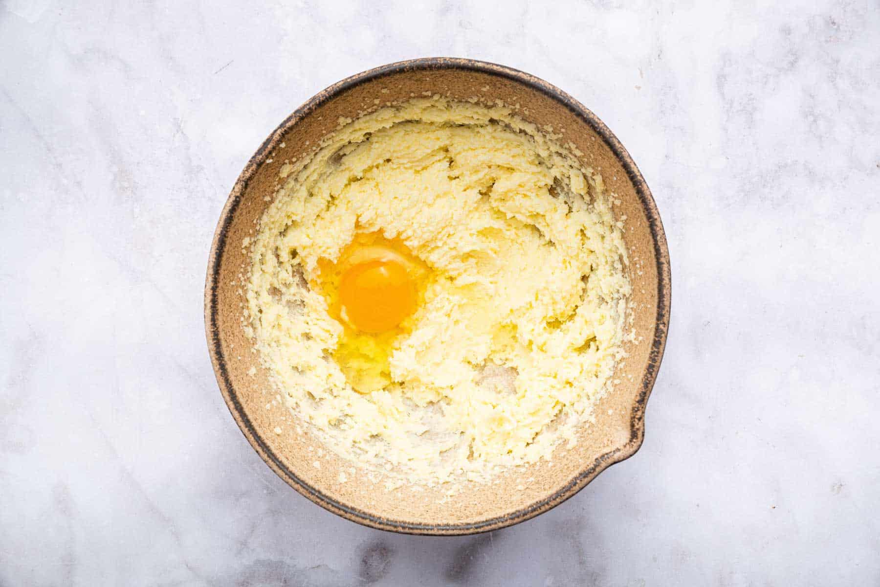 Raw egg on top of yellow cake batter in brown bowl.