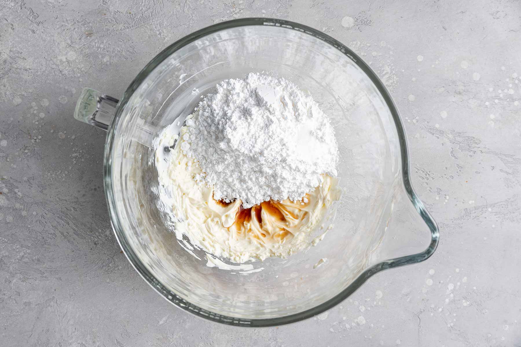 Adding powdered sugar and vanilla to cream cheese frosting in bowl.