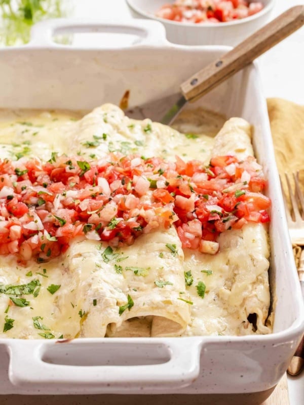 Pan of white chicken enchiladas with pico de gallo on top.