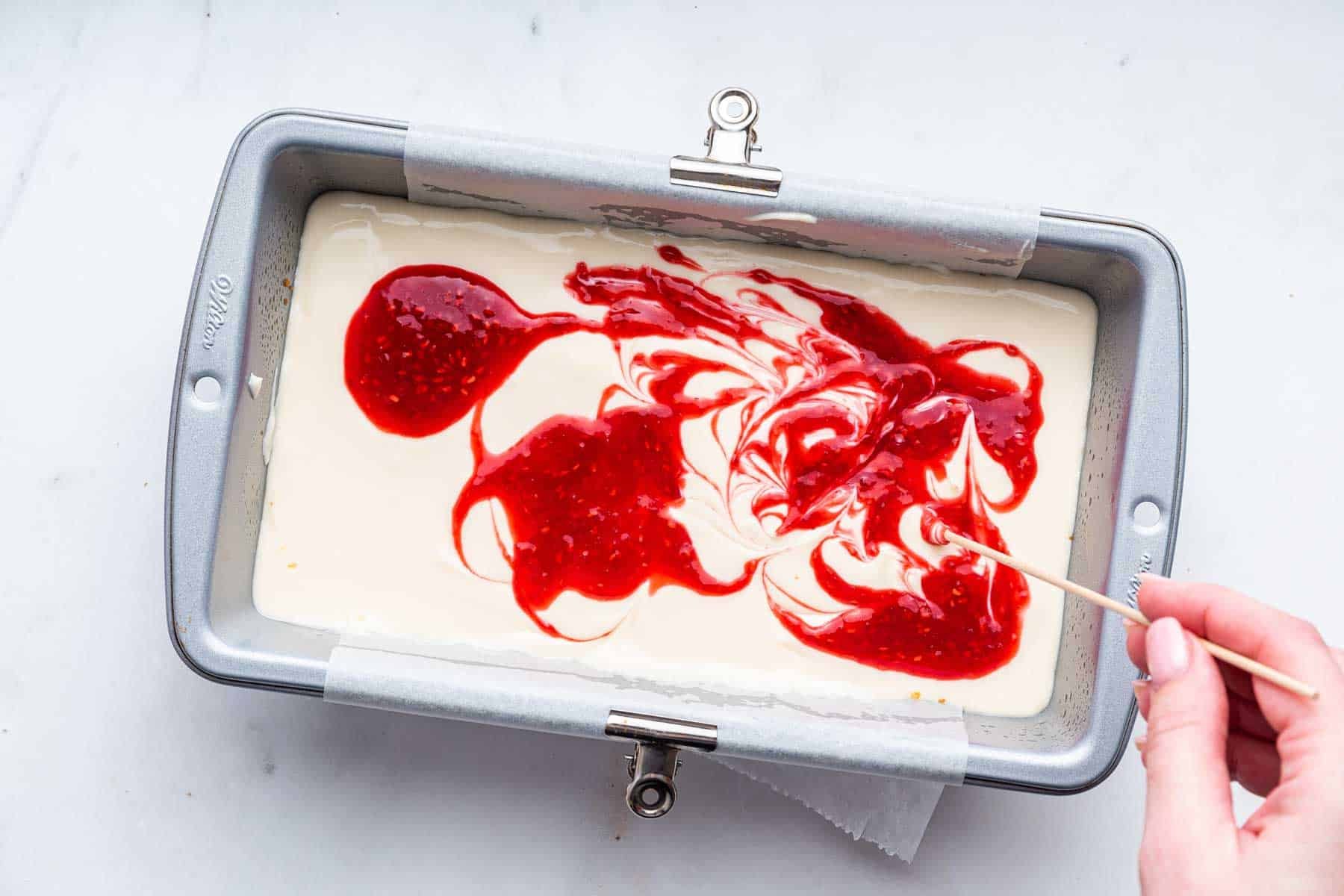 White batter with bright red sauce being swirled in with a toothpick.