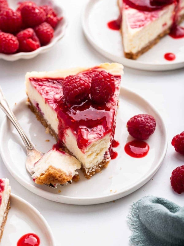 Slice of bright red raspberry white chocolate cheesecake with first bite missing on fork.